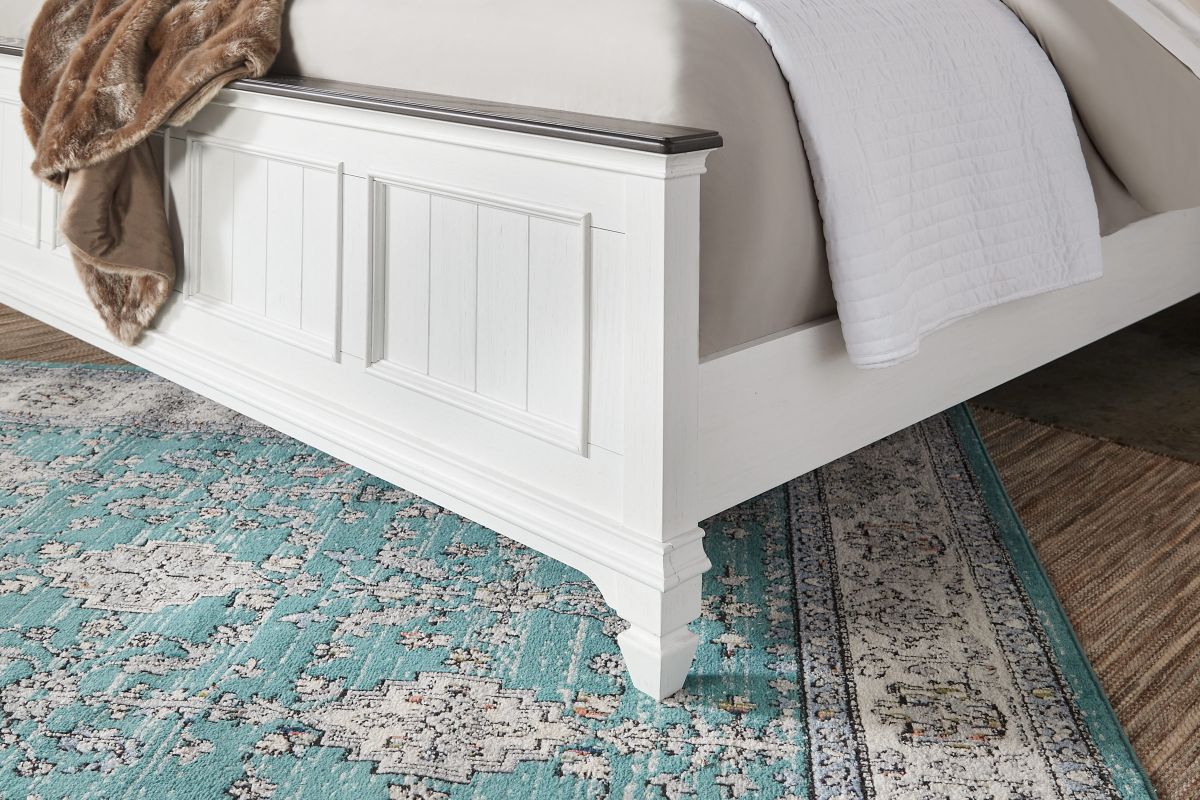 A close up image of the corner of a white footboard on a light blue rug